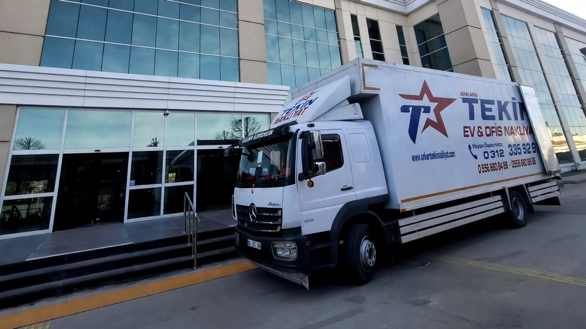 Tekin Nakliyat kamyonu cam cepheli ofis binasının önünde ofis taşıması için yanaşmış